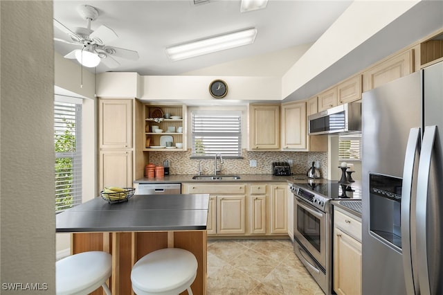 kitchen featuring ceiling fan, sink, stainless steel appliances, vaulted ceiling, and a kitchen bar