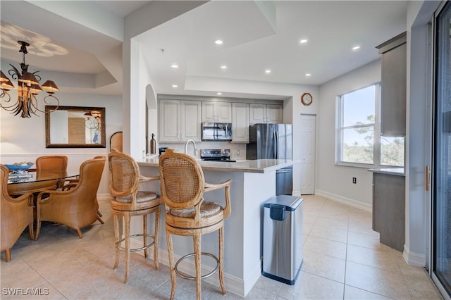 kitchen with kitchen peninsula, a chandelier, a breakfast bar area, gray cabinets, and appliances with stainless steel finishes