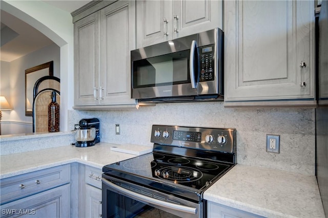 kitchen with tasteful backsplash, gray cabinetry, light stone counters, and black range with electric cooktop