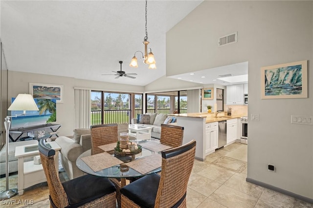 tiled dining area featuring ceiling fan with notable chandelier, high vaulted ceiling, and sink