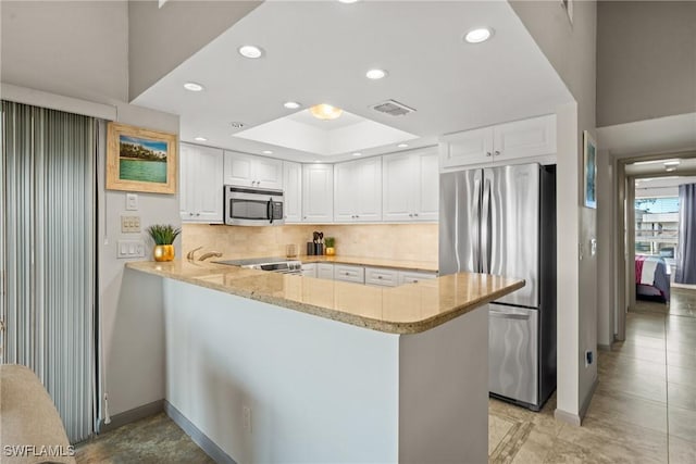 kitchen with a peninsula, visible vents, appliances with stainless steel finishes, light stone countertops, and a tray ceiling