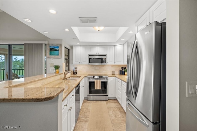 kitchen featuring kitchen peninsula, appliances with stainless steel finishes, light stone countertops, sink, and white cabinets