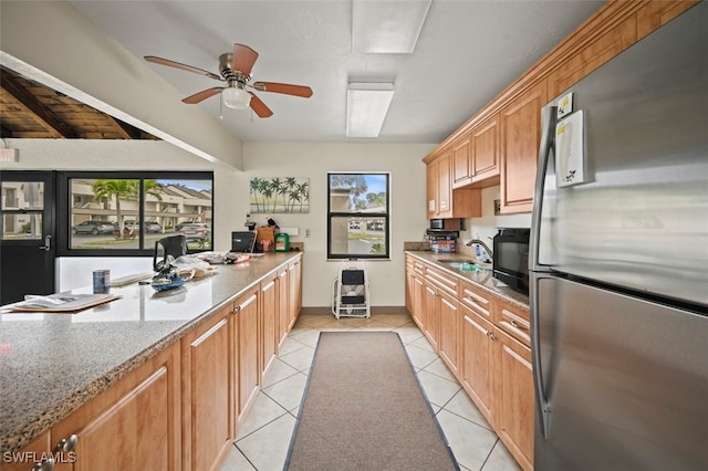 kitchen with light tile patterned floors, a ceiling fan, freestanding refrigerator, light stone countertops, and a sink