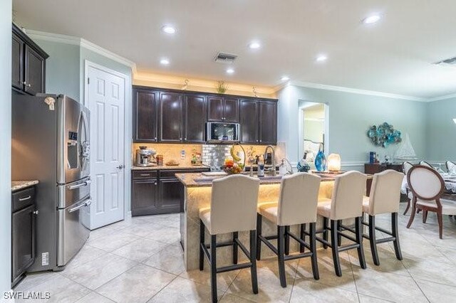 kitchen featuring stainless steel fridge, ornamental molding, a breakfast bar, dark brown cabinets, and an island with sink