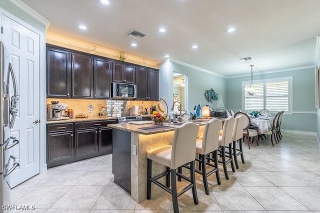 kitchen featuring pendant lighting, a kitchen breakfast bar, crown molding, an island with sink, and appliances with stainless steel finishes