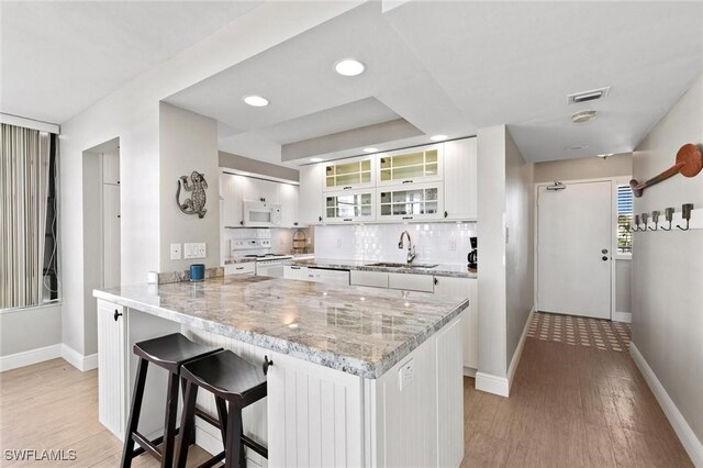 kitchen with sink, white appliances, kitchen peninsula, and white cabinets