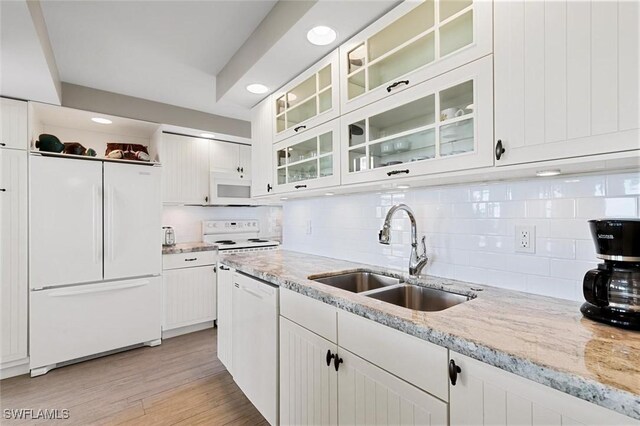 kitchen with white cabinetry, sink, decorative backsplash, light stone counters, and white appliances