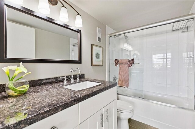 full bathroom featuring vanity, combined bath / shower with glass door, and toilet