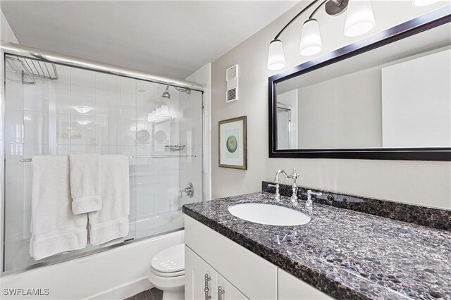 full bathroom with bath / shower combo with glass door, vanity, and toilet