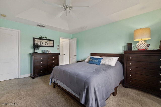 carpeted bedroom with ceiling fan and a tray ceiling