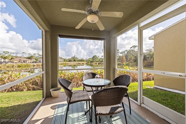 sunroom with ceiling fan and a water view