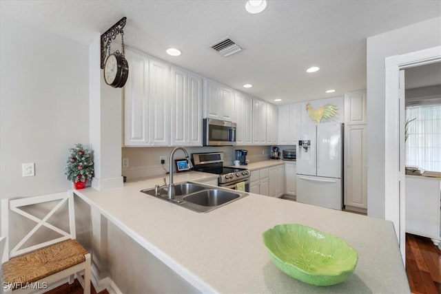 kitchen featuring kitchen peninsula, appliances with stainless steel finishes, dark hardwood / wood-style flooring, sink, and white cabinets