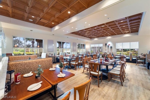 dining room featuring light wood-type flooring, a towering ceiling, and coffered ceiling