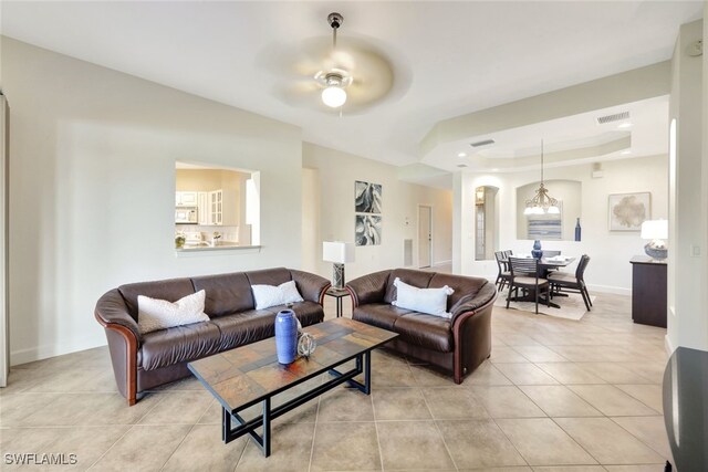 living room with light tile patterned floors, ceiling fan with notable chandelier, and a raised ceiling