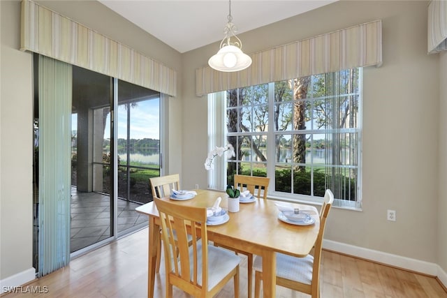 dining area featuring baseboards, a water view, and light wood finished floors