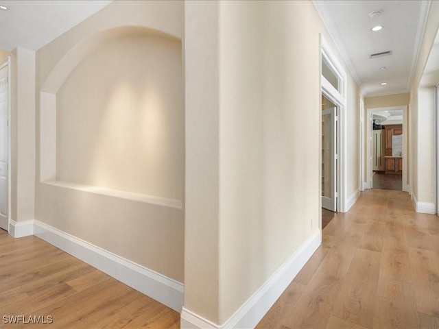 hall with light wood-type flooring and ornamental molding