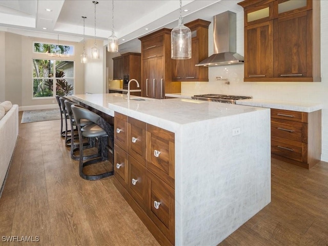 kitchen with wall chimney exhaust hood, hanging light fixtures, a spacious island, stainless steel gas stovetop, and a kitchen bar