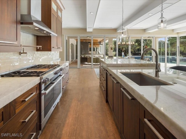 kitchen featuring beam ceiling, wall chimney range hood, light stone counters, pendant lighting, and range with two ovens