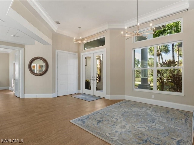 entryway featuring french doors, a wealth of natural light, crown molding, an inviting chandelier, and hardwood / wood-style floors