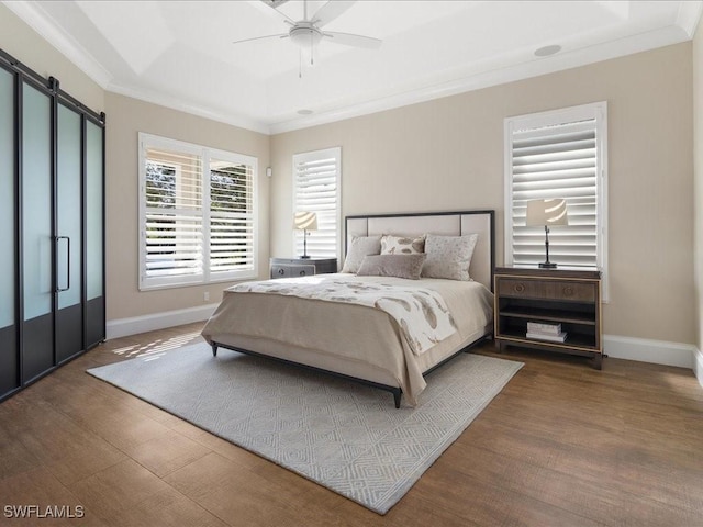 bedroom with dark hardwood / wood-style flooring, a tray ceiling, ceiling fan, crown molding, and a barn door