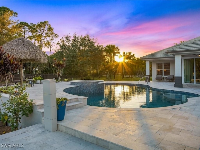 pool at dusk featuring an in ground hot tub and a patio