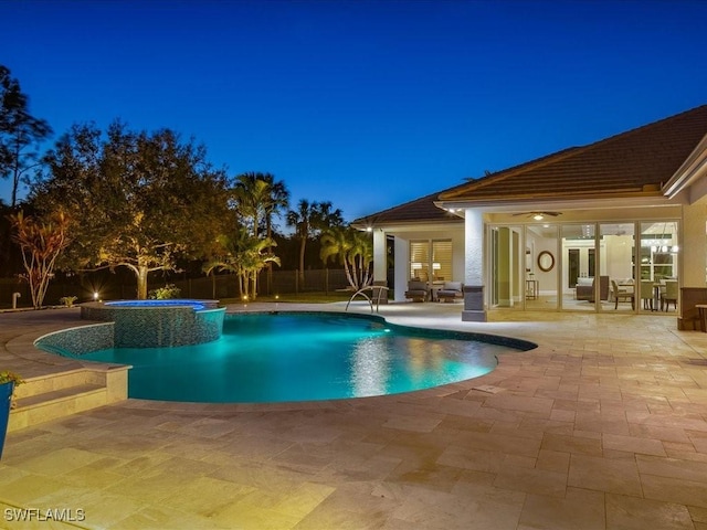 pool at night featuring an in ground hot tub and a patio