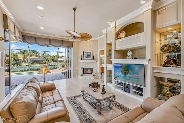 living room with ceiling fan, a large fireplace, light tile patterned flooring, and crown molding