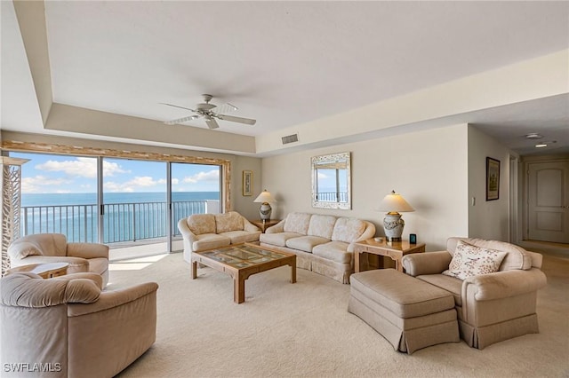 carpeted living room with a raised ceiling, ceiling fan, and a water view