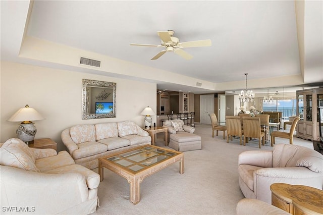 living room with ceiling fan with notable chandelier, a raised ceiling, and light colored carpet