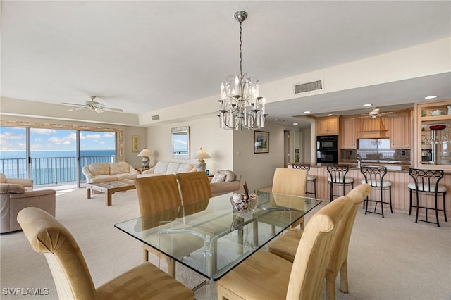 carpeted dining area featuring ceiling fan with notable chandelier and a water view