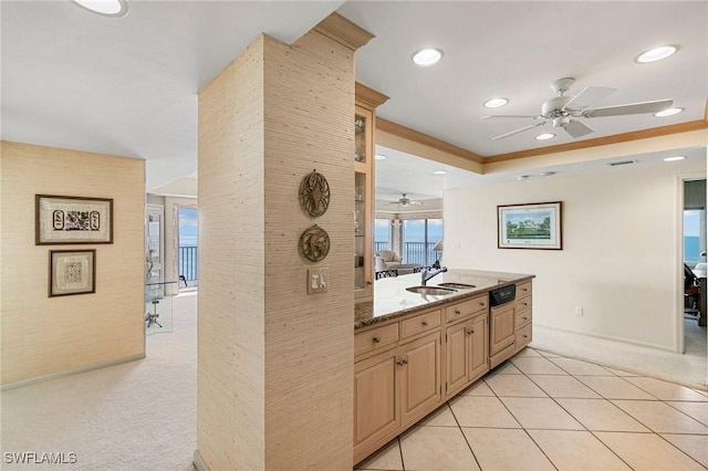 kitchen with sink, dark stone countertops, a tray ceiling, light carpet, and light brown cabinetry