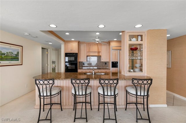 kitchen with ceiling fan, double oven, paneled built in refrigerator, dark stone countertops, and a breakfast bar area