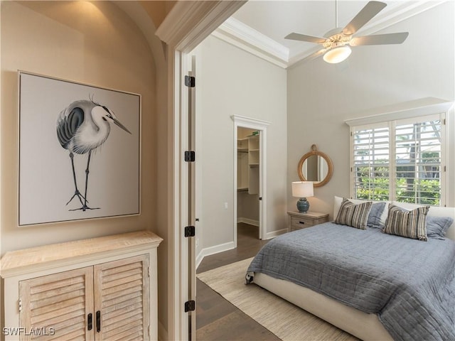 bedroom with a spacious closet, ceiling fan, wood-type flooring, a closet, and crown molding