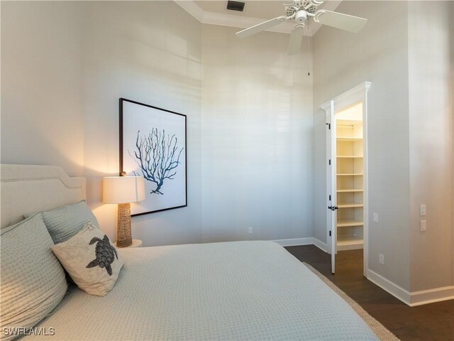 bedroom with dark wood-type flooring, a closet, crown molding, a walk in closet, and ceiling fan