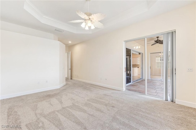 carpeted empty room featuring a raised ceiling, ceiling fan, and crown molding