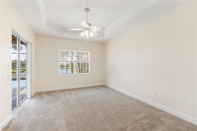 carpeted empty room featuring ornamental molding, a raised ceiling, ceiling fan, and a healthy amount of sunlight