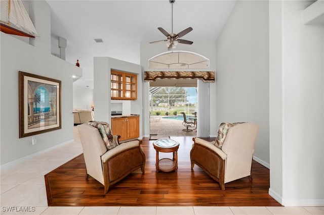 sitting room with ceiling fan, light tile patterned floors, and a towering ceiling