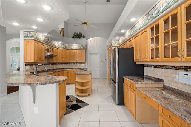 kitchen featuring ceiling fan, kitchen peninsula, dark stone countertops, a breakfast bar, and light tile patterned floors