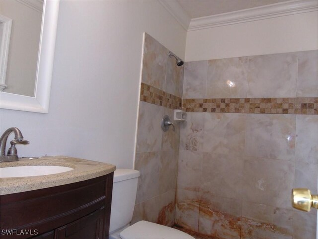 bathroom featuring toilet, a tile shower, ornamental molding, and vanity