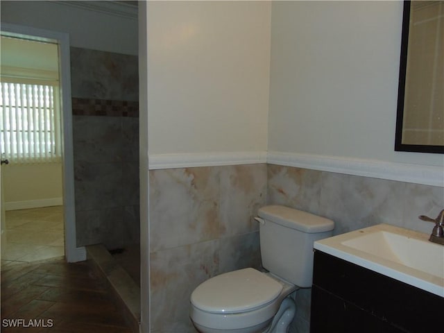 bathroom with vanity, toilet, ornamental molding, tiled shower, and tile walls