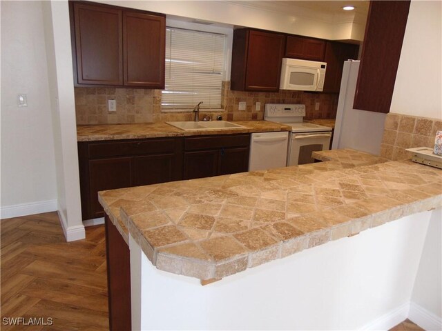 kitchen featuring kitchen peninsula, decorative backsplash, white appliances, dark brown cabinetry, and sink