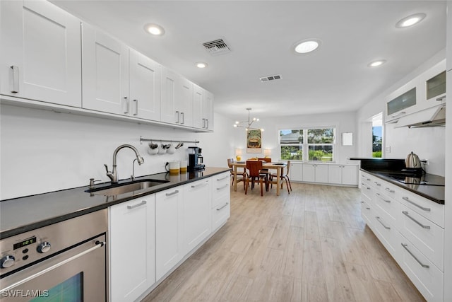 kitchen with black electric stovetop, sink, an inviting chandelier, white cabinets, and light hardwood / wood-style floors