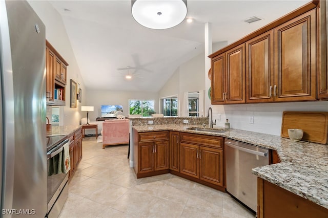 kitchen featuring light stone countertops, vaulted ceiling, sink, kitchen peninsula, and stainless steel appliances