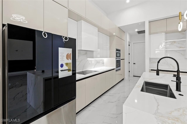 kitchen featuring pendant lighting, black appliances, sink, light stone counters, and white cabinetry