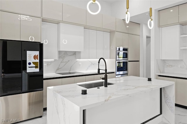 kitchen featuring a kitchen island with sink, sink, appliances with stainless steel finishes, tasteful backsplash, and decorative light fixtures