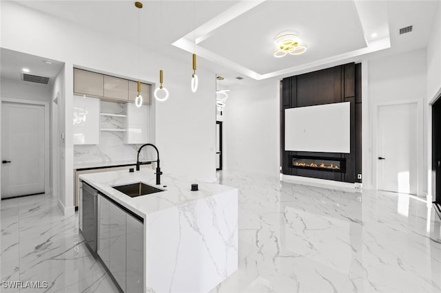 kitchen featuring a large fireplace, sink, hanging light fixtures, a raised ceiling, and light stone counters