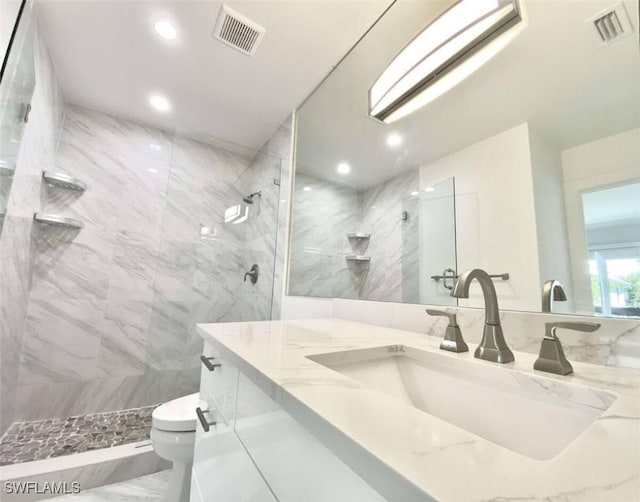 bathroom with tiled shower, vanity, tile walls, and toilet