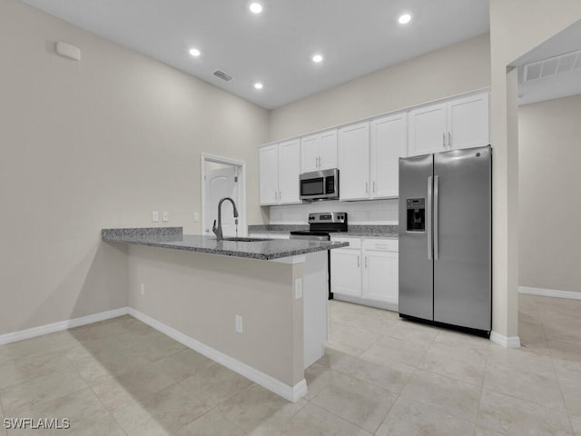 kitchen featuring white cabinetry, sink, stainless steel appliances, kitchen peninsula, and dark stone countertops