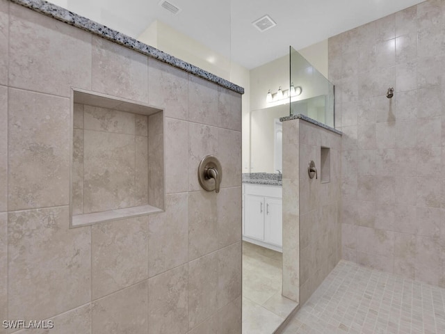 bathroom with tile patterned flooring, vanity, a tile shower, and tile walls