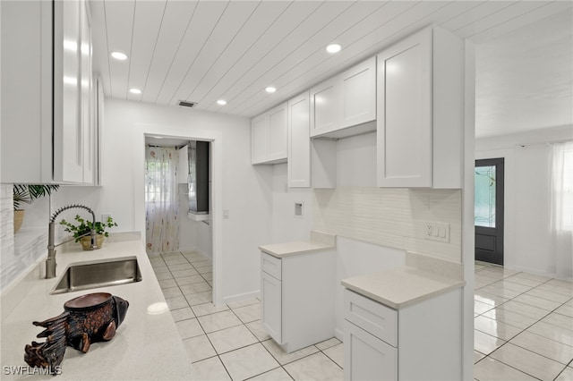 kitchen featuring white cabinets, backsplash, light tile patterned floors, and sink